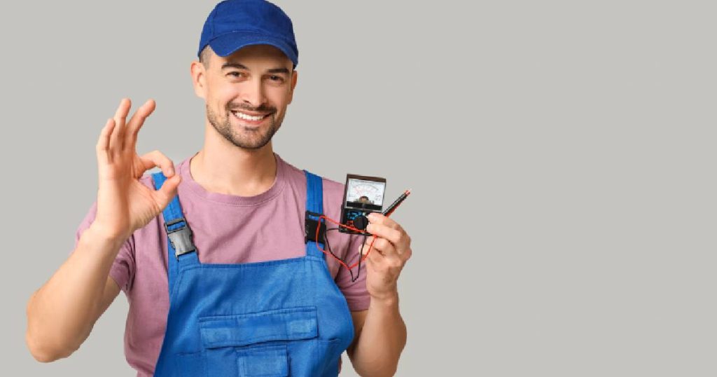 Een elektricien met een roze t-shirt en een blauwe pet en overall heeft een spanningsmeter vast: een apparaatje dat hij nodig heeft om te bepalen hoeveel stroom er op een elektrische aansluiting staat. 