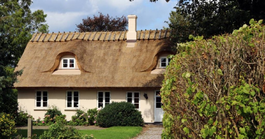 Een huis met een strak gelegde rieten dak. Het erf heeft een tuin en een aantal bomen en struiken.