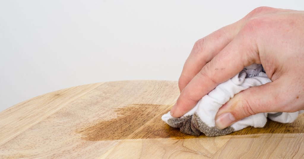 Een hand behandelt een lichtgekleurde houten trap met beits.